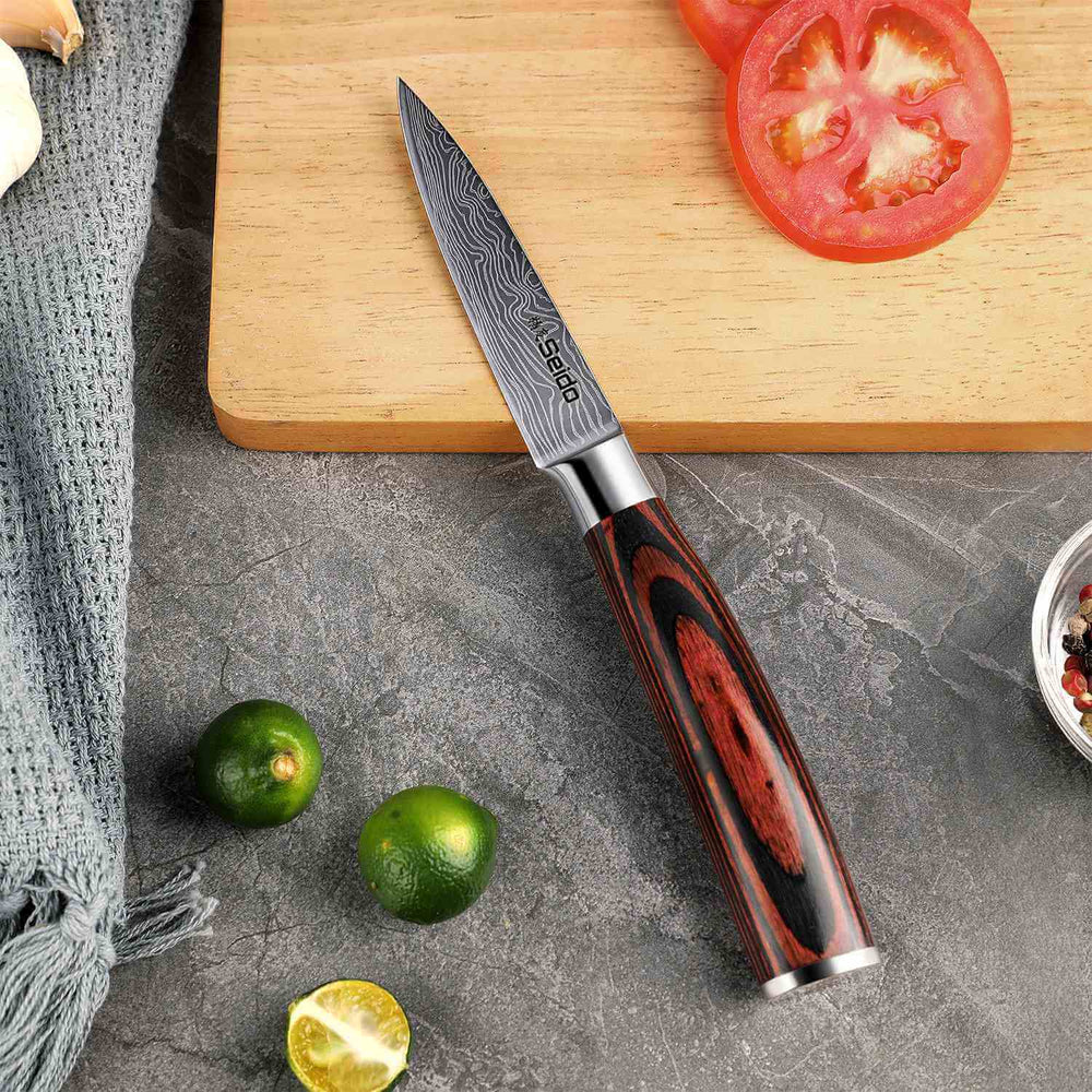 Knife with a wooden handle on a cutting board with sliced tomatoes and limes.