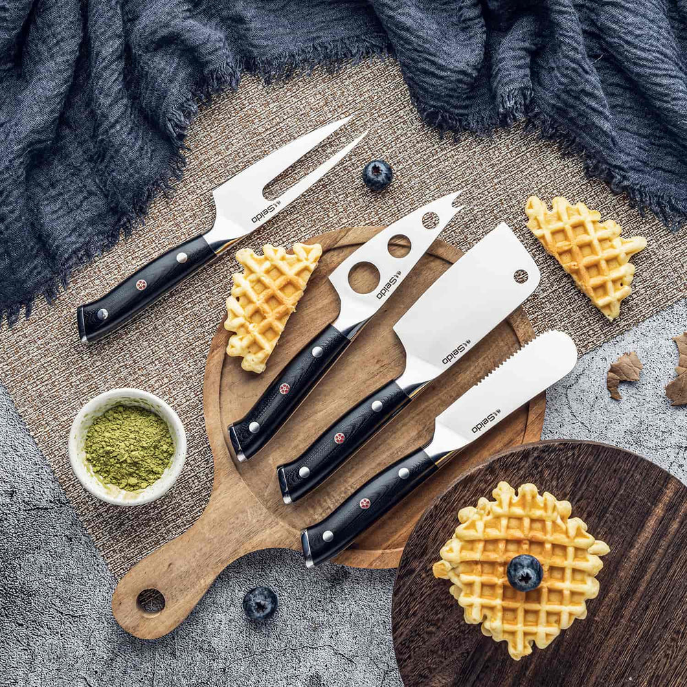 Set of four cheese knives on a wooden board with waffles and blueberries.