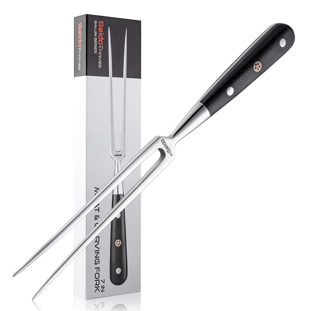Carving fork with black handle and silver blade next to its packaging on a white background