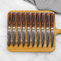Set of ten knives with wooden handles on a wooden board against a marble background