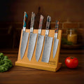 Set of 5 shink series knives on a wooden magnetic stand with a tomato and leafy greens on a wooden surface.