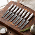 8 Takoizu serrated Damascus steak knives with white turquoise handles on an acacia cutting board