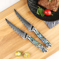 Awabi serrated steak knives with Damascus blades and abalone shell resin handles on a cutting board near a piece of meat.