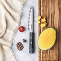Epokishi AUS-10 damascus knife on a marble surface with sliced fruit and a wooden cutting board.