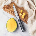 Mango half and cubed pieces on a wooden cutting board with a 5-inch epokishi petty knife, on a light fabric background.
