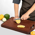 Person slicing lemons on a wooden cutting board with vegetables in the background