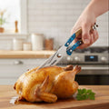 Person cutting a roasted chicken with the blue-resin handled Executives series kitchen sheas, on a wooden cutting board in a kitchen.