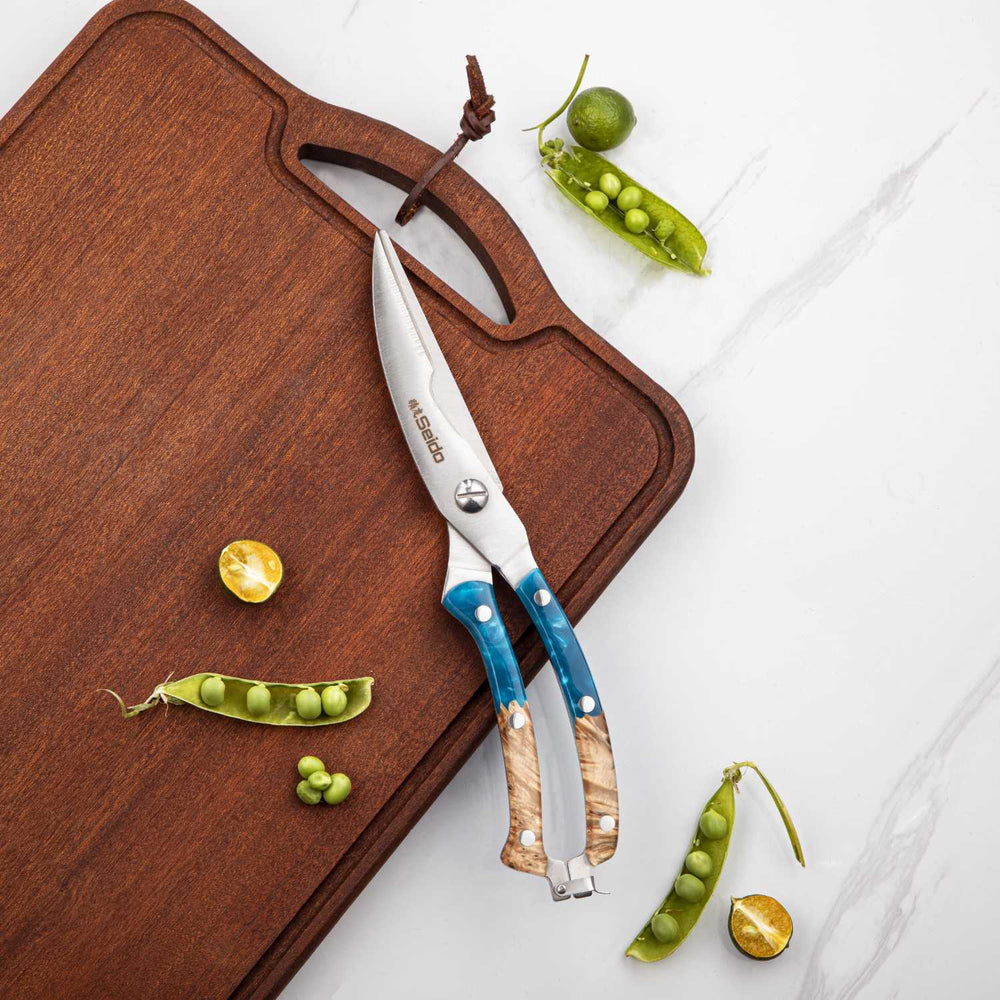 Butterfly kitchen shears with blue handles on a wooden cutting board with green peas.