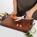 Person cutting chicken on a wooden cutting board with a pair of kitchen scissors.