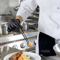 Chef using fine tip tweezers to set food on a plat, in a professional kitchen.