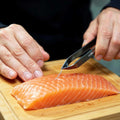 Person removing a fish bone from a salmon fillet with a Fish-Bone Tweezer on a wooden cutting board.