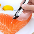 Hand using a metal Fish-Bone Tweezer on a piece of salmon with lemons in the background.
