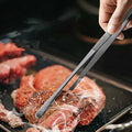 Using flat tip tweezers to turn a seared steak in a hot pan.