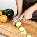 Person slicing a lime with an Inferuno Series 3.5 inch Paring Knife on a wooden cutting board, surrounded by fruits.