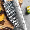 Close-up view of the Kanpeki cleaver blade, detail showing hammered top and Damascus cladding, near fruits.