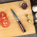 Knife on a wooden cutting board with sliced tomatoes, limes, and peppercorns.