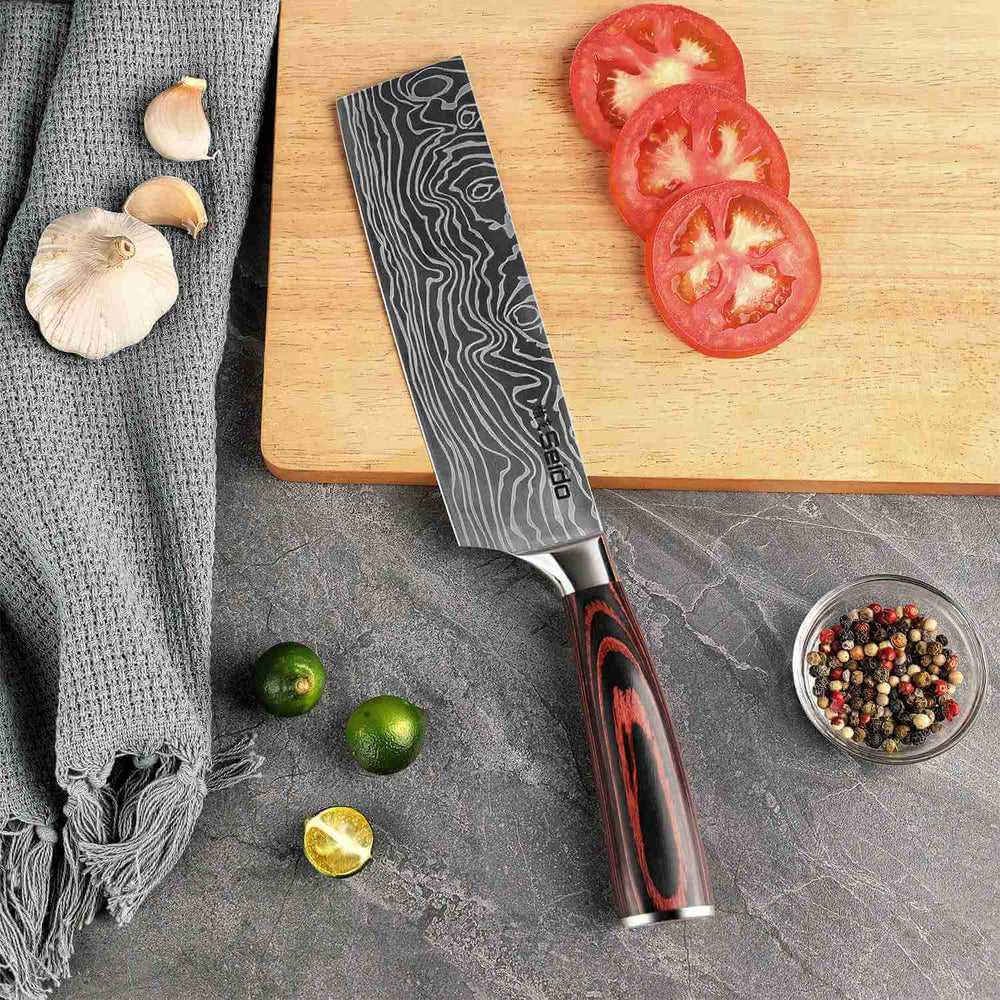 Chef's knife with a decorative blade pattern on a kitchen counter with vegetables and a cutting board.