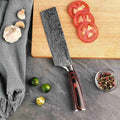 Chef's knife with a decorative blade pattern on a kitchen counter with vegetables and a cutting board.