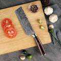 Knife on a wooden cutting board with sliced tomatoes, limes, and garlic on a dark surface.