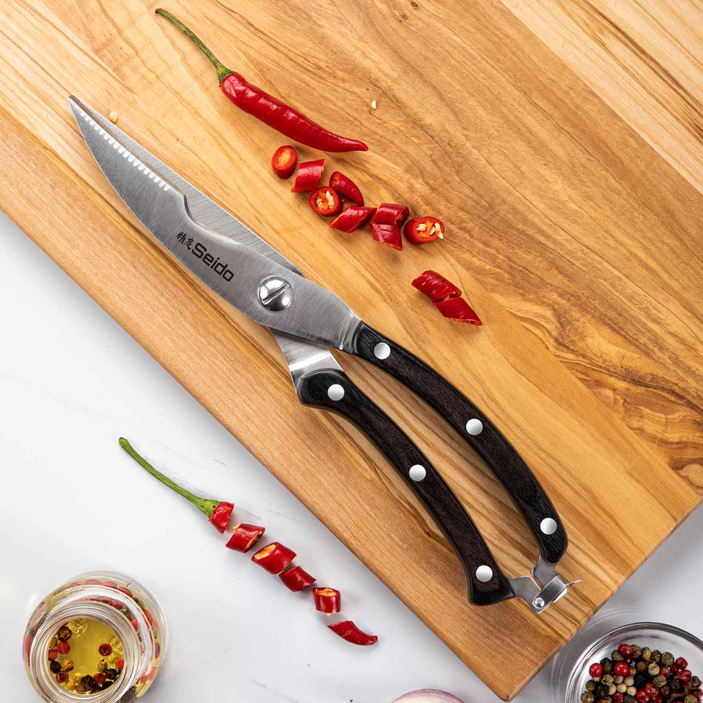 Serrated knife with black handle on a wooden cutting board with red chili peppers.