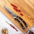 Serrated knife with black handle on a wooden cutting board with red chili peppers.