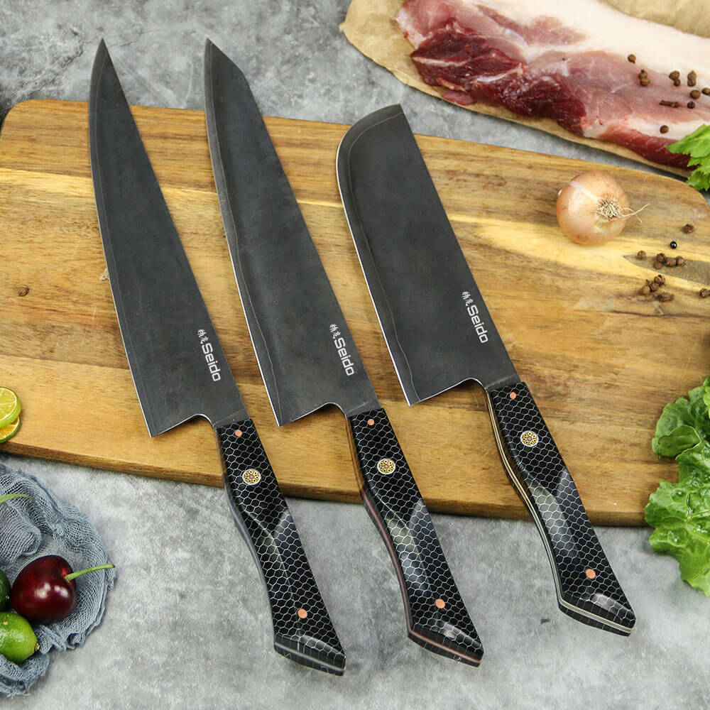 Three knives on a cutting board with vegetables and meat. Moretsuna Japanese Knife Set by Seido Knives.