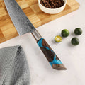 Shinko Chef's knife with a decorative maple & resin handle, with a polished bolster on a kitchen counter with limes and coffee beans. 