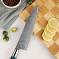 Shinko Chef's knife with a 110 layer Damascus steel blade on a wooden cutting board with lemons and limes.