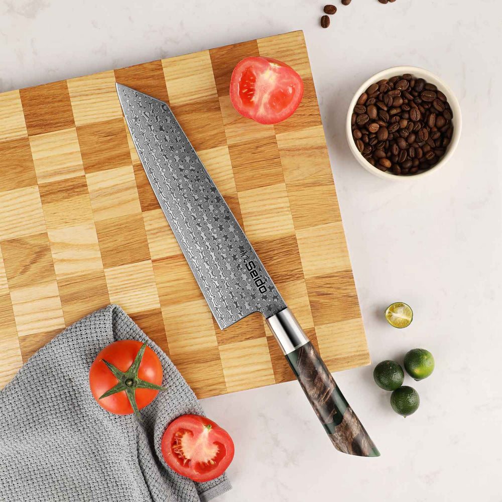 Kiritsuke knife on a wooden cutting board with tomatoes and coffee beans on a light surface