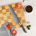 Kiritsuke knife on a wooden cutting board with tomatoes and coffee beans on a light surface