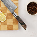Handle detail of Shinko Kiritsuke with resin and stabilized maple, on a cutting board next to lemon slices and coffee beans.
