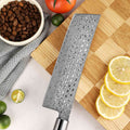 Close-up of the Shinko Nakiri Damascus blade, on a wooden cutting board with lemons, limes, and coffee beans.