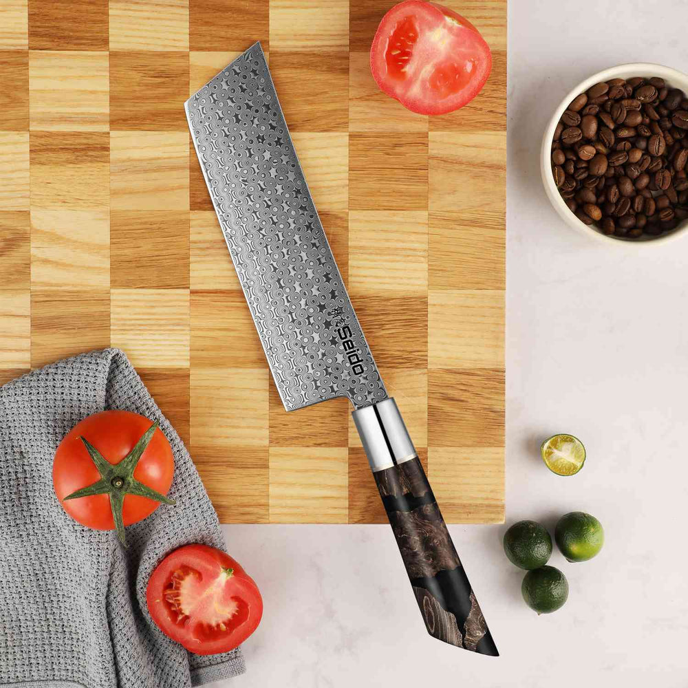 Chef's knife on a wooden cutting board with tomatoes and limes