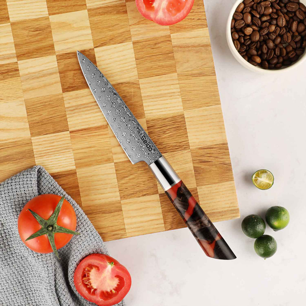 Japanese Petty knife with a decorative resing handle on a wooden cutting board with tomatoes and limes.