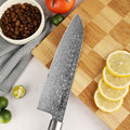 Close-up Damascus pattern on Shinko Santoku, on a wooden cutting board with lemons and coffee beans.