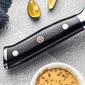 Shujin series handle close-up showing black G10 fiberglass with mosaic pin and polished rivets.