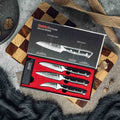 Shujin 3-piece paring knife set shown with gift box and three sheaths on wooden cutting board with a checkered pattern.