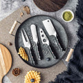 Set of knives on a dark gray plate with waffles and pinecones on a textured surface