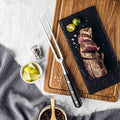 Shujin Series Meat & Carving Fork resting on a board beside sliced steak.