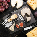 Assorted cheeses and figs on a black slate board with cheese knives.