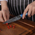 Person using a damascus knife to cut red peppers on a wooden cutting board.