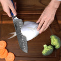 Person using a Santoku knife to cut fish on a wooden cutting board with vegetables.