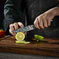 Person slicing a lime with a utility knife on a wooden cutting board.