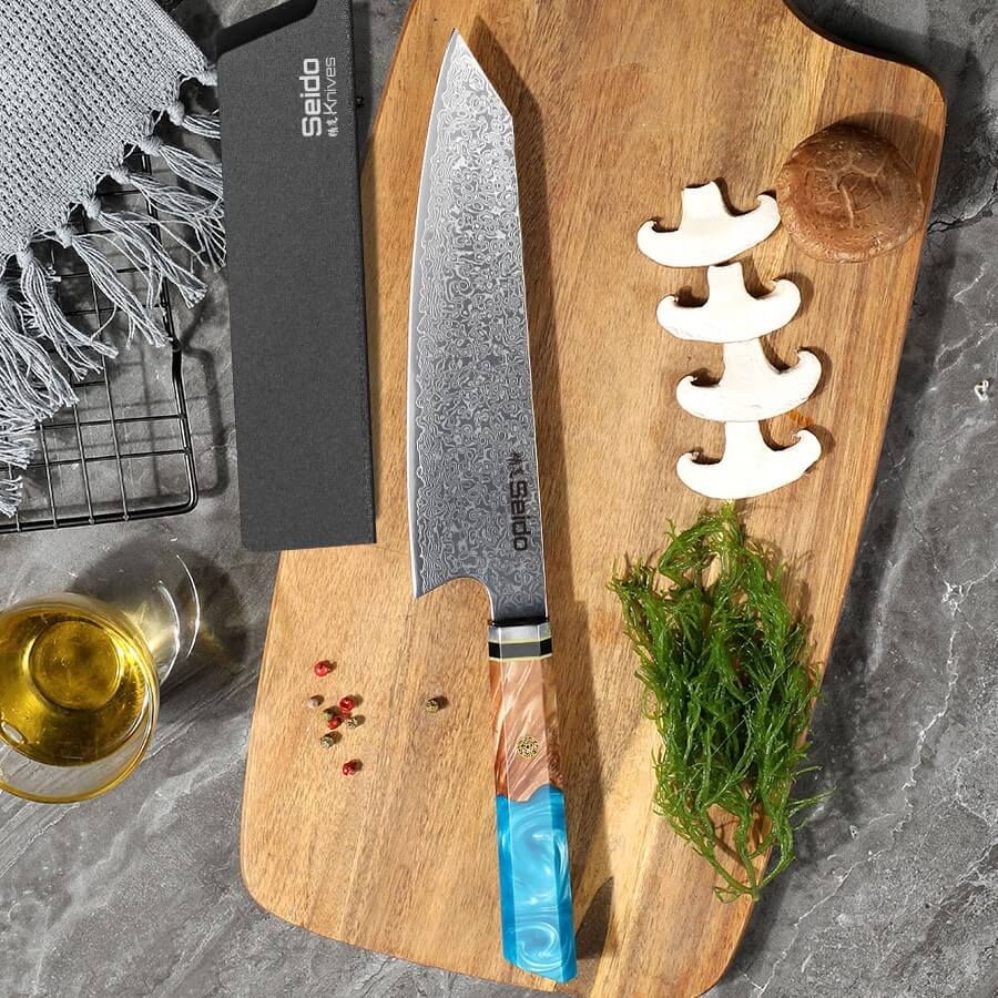 Enhance your skills with the Kiritsuke Damascus Chef Knife from Seido Knives, accompanied by herbs on a cutting board.