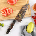 Overhead view of the Kurogane 7-inch Bunka knife with rainbow Damascus blade beside tomatoes and citrus