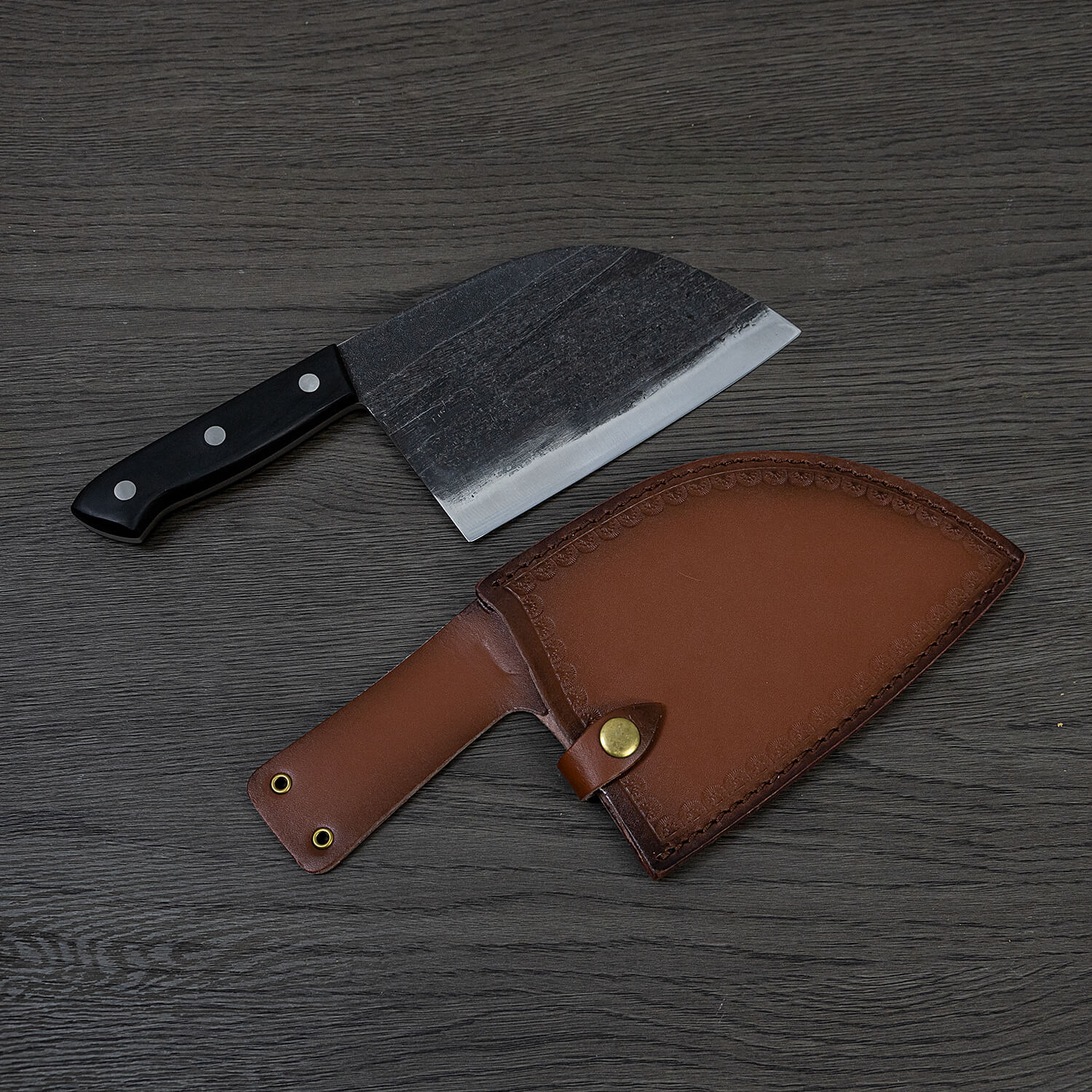 Enhance your kitchen with a Serbian Cleaver Knife accompanied by a leather sheath, beautifully displayed on a table.