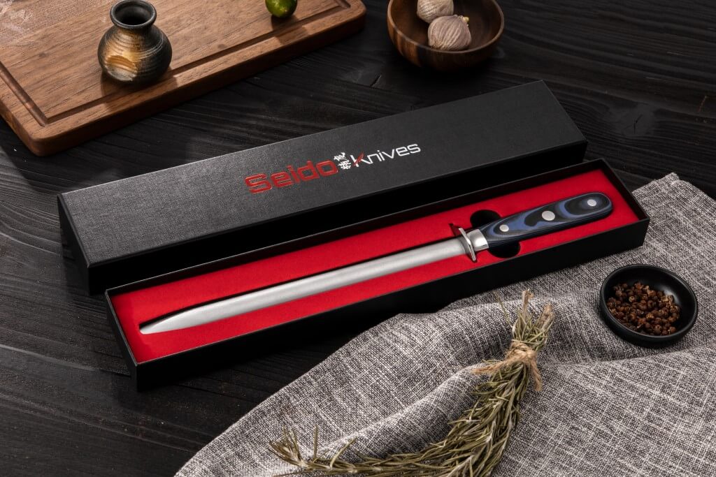 A sleek black box holds a sharp knife and herbs, accompanied by the Kanpeki Diamond Sharpening Rod from Seido Knives.