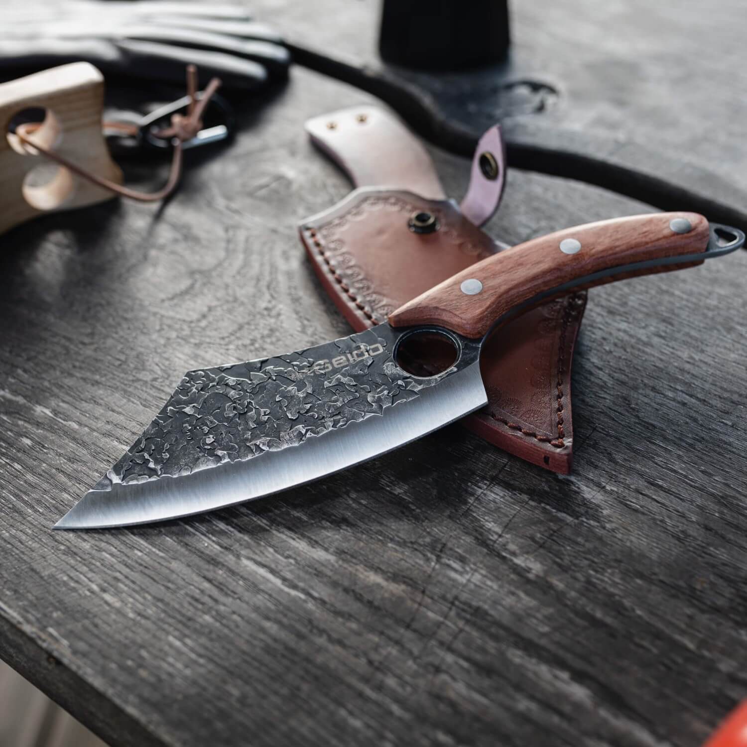 Behold the Hakai Cleaver Knife, a masterpiece from Seido Knives, resting on a table with its protective leather sheath.