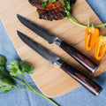 Seido Knives' serrated steak knives on a cutting board, ready to slice through a juicy piece of meat and a vibrant pepper.