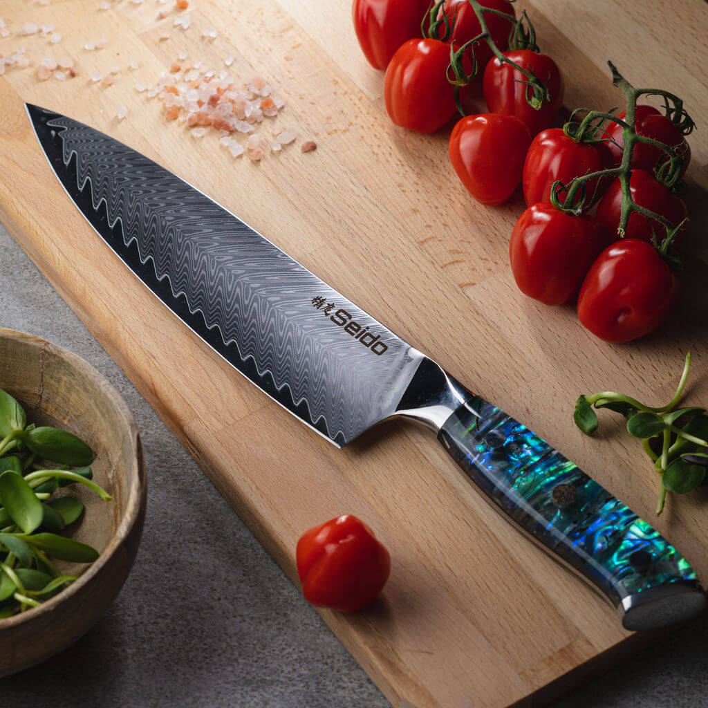 A stunning Awabi Gyuto Damascus Steel Chef Knife by Seido Knives, resting on a cutting board with fresh tomatoes.